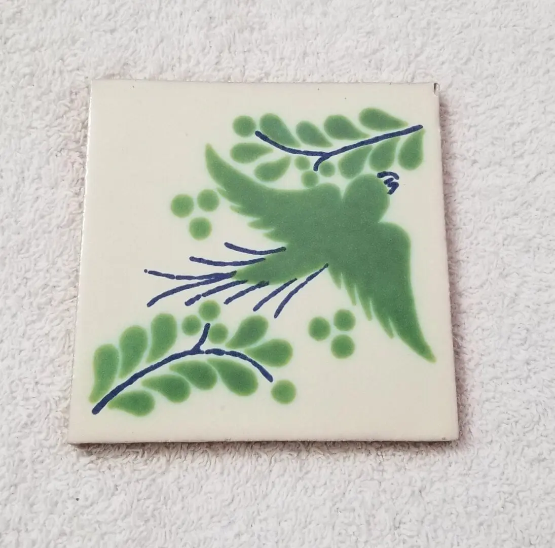 Decorative ceramic tile with green bird and foliage design.