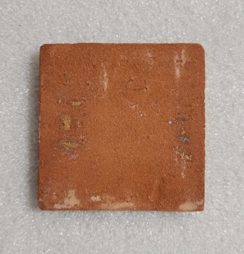 A worn, square red clay tile on a light background.