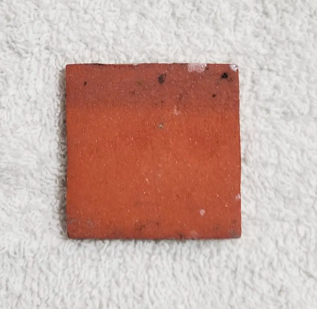 Square red tile on a textured white surface.