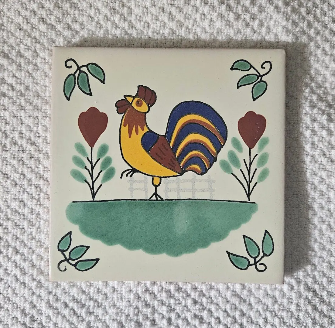 Decorative tile with a colorful rooster and floral motifs.