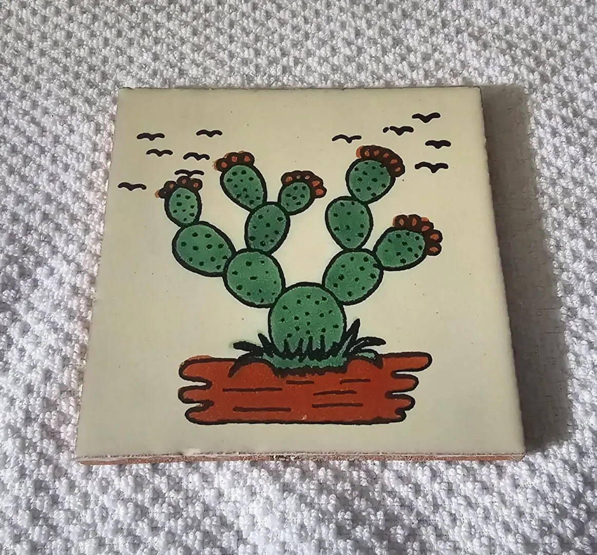 Tile with cactus illustration on textured fabric.