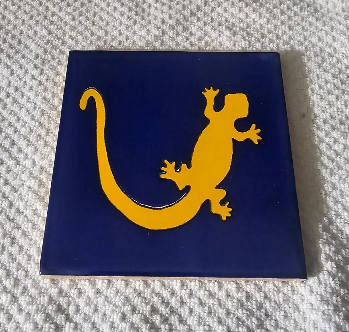 Square tile with a yellow gecko silhouette on a blue background.