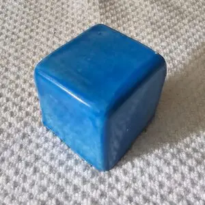 A smooth, blue, cube-shaped stone on a textured surface.