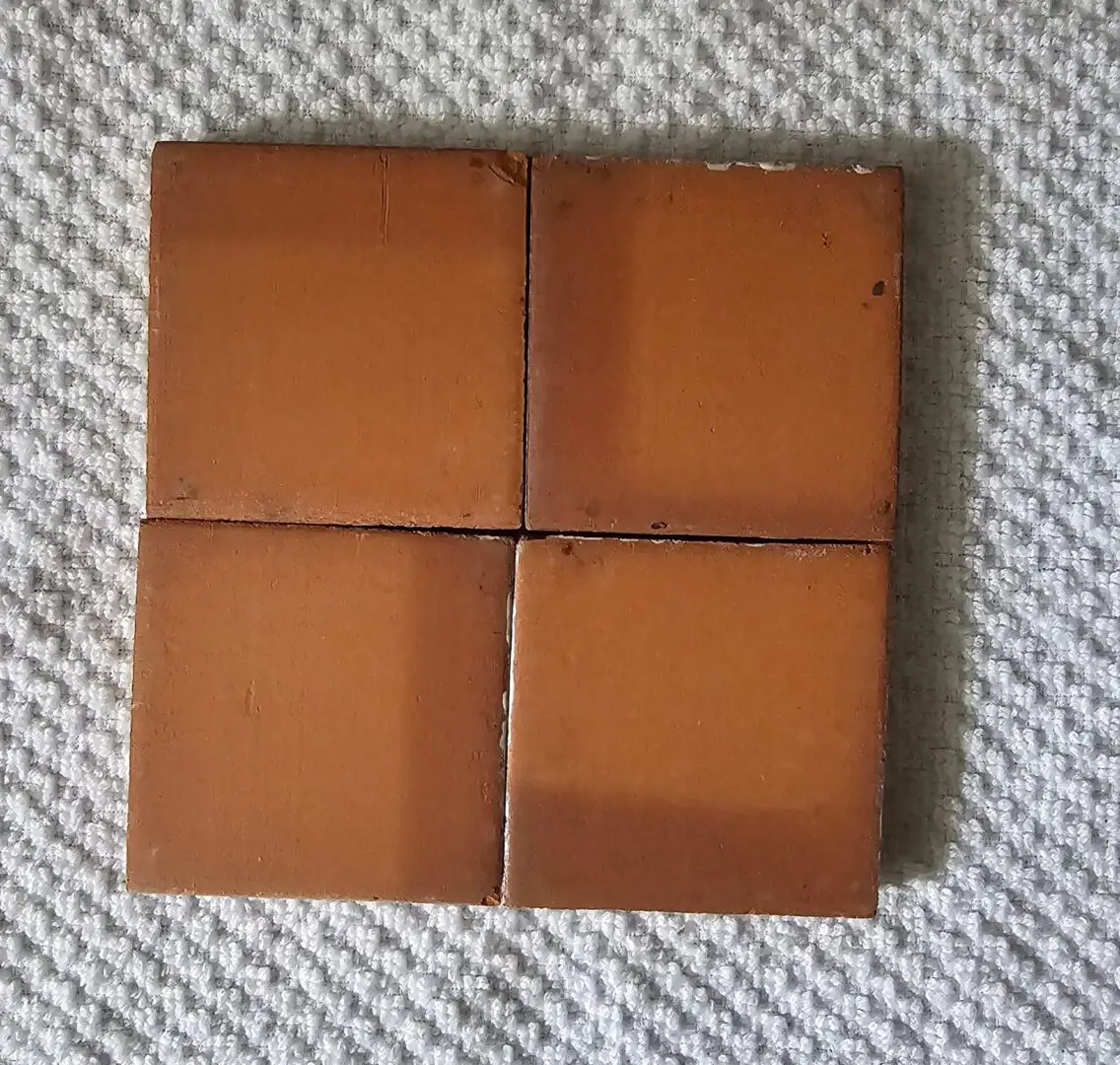 Four square brown leather coasters with worn edges on a textured fabric surface.
