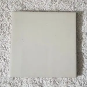 A blank, square, off-white tile on a textured surface.