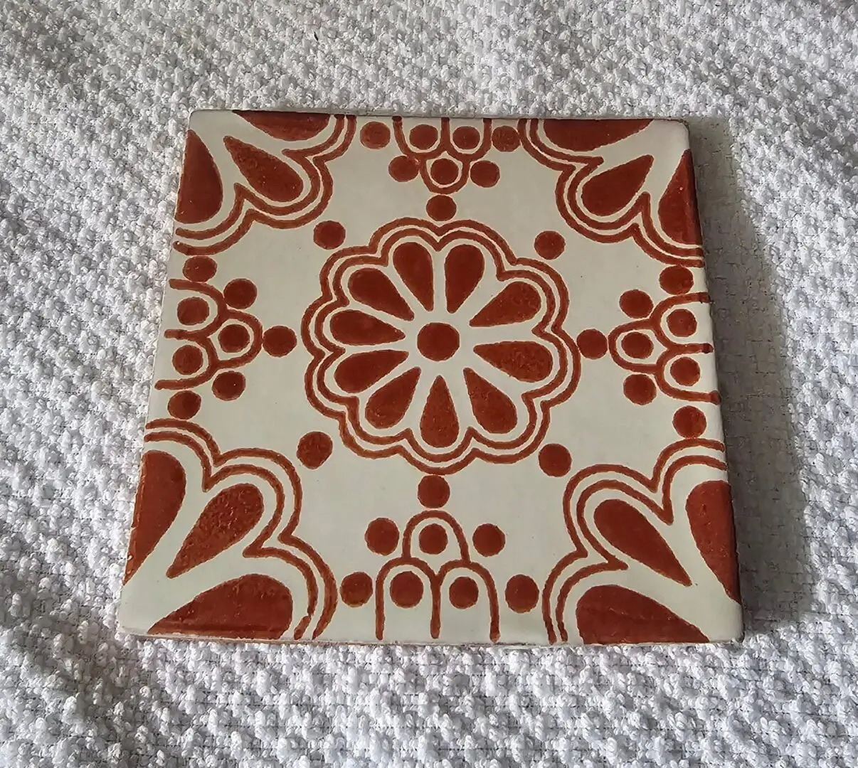 Decorative square tile with red floral and heart patterns on cream background.