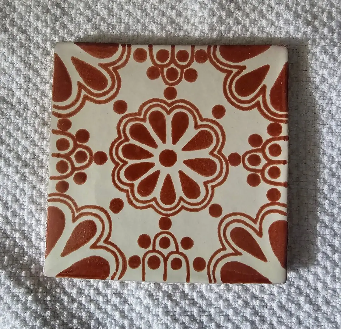 Decorative ceramic tile with a red floral pattern on white background.