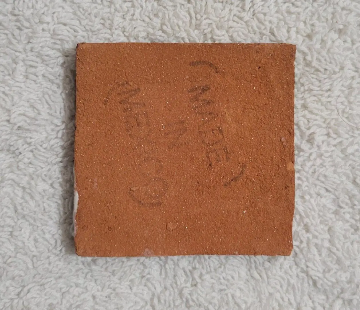 Square terracotta tile with faint handwriting