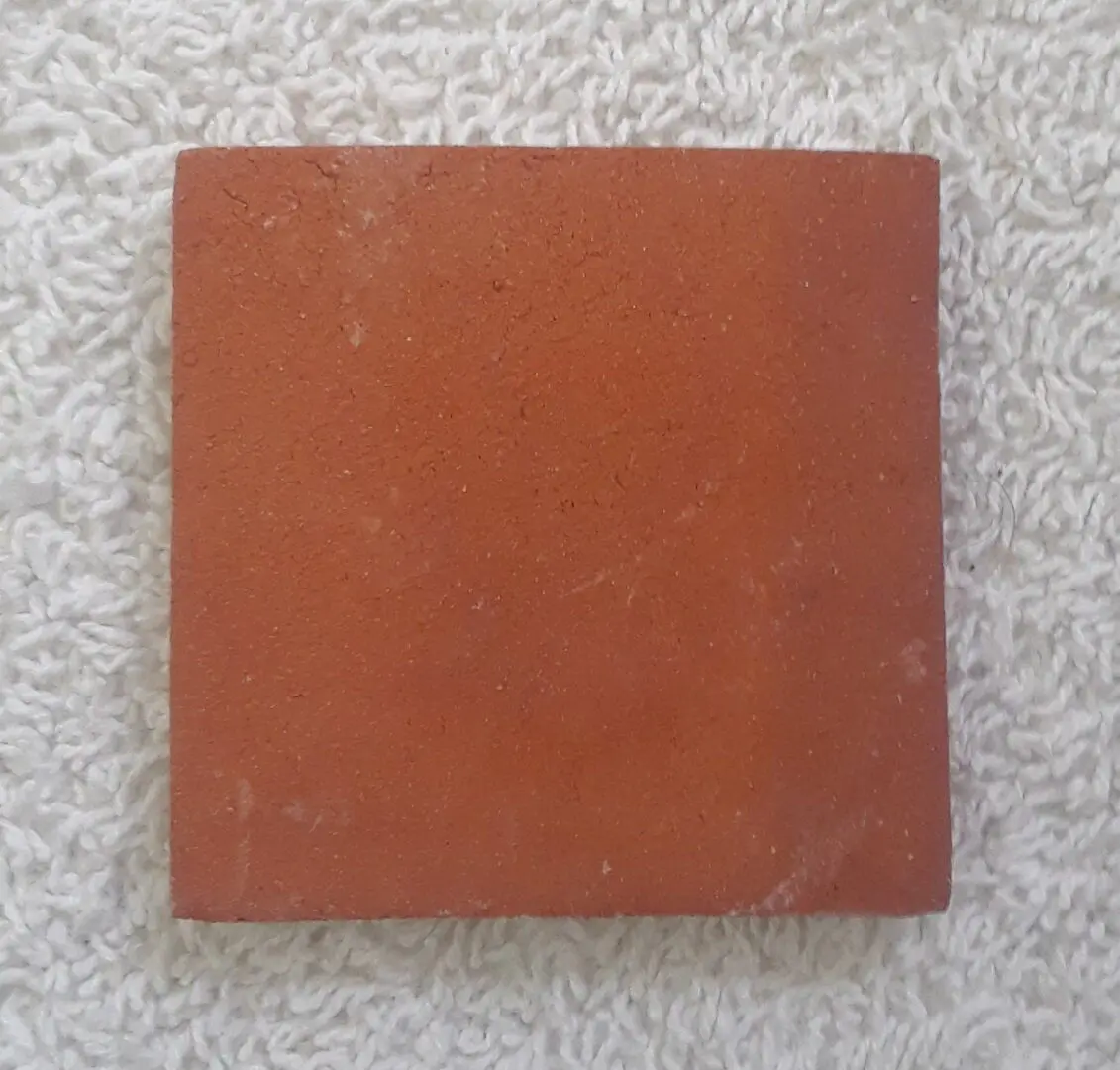 A single square terracotta tile on a light carpet.