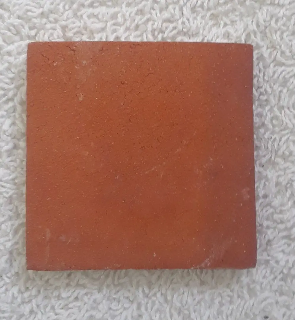 A square reddish-brown tile on a speckled surface.