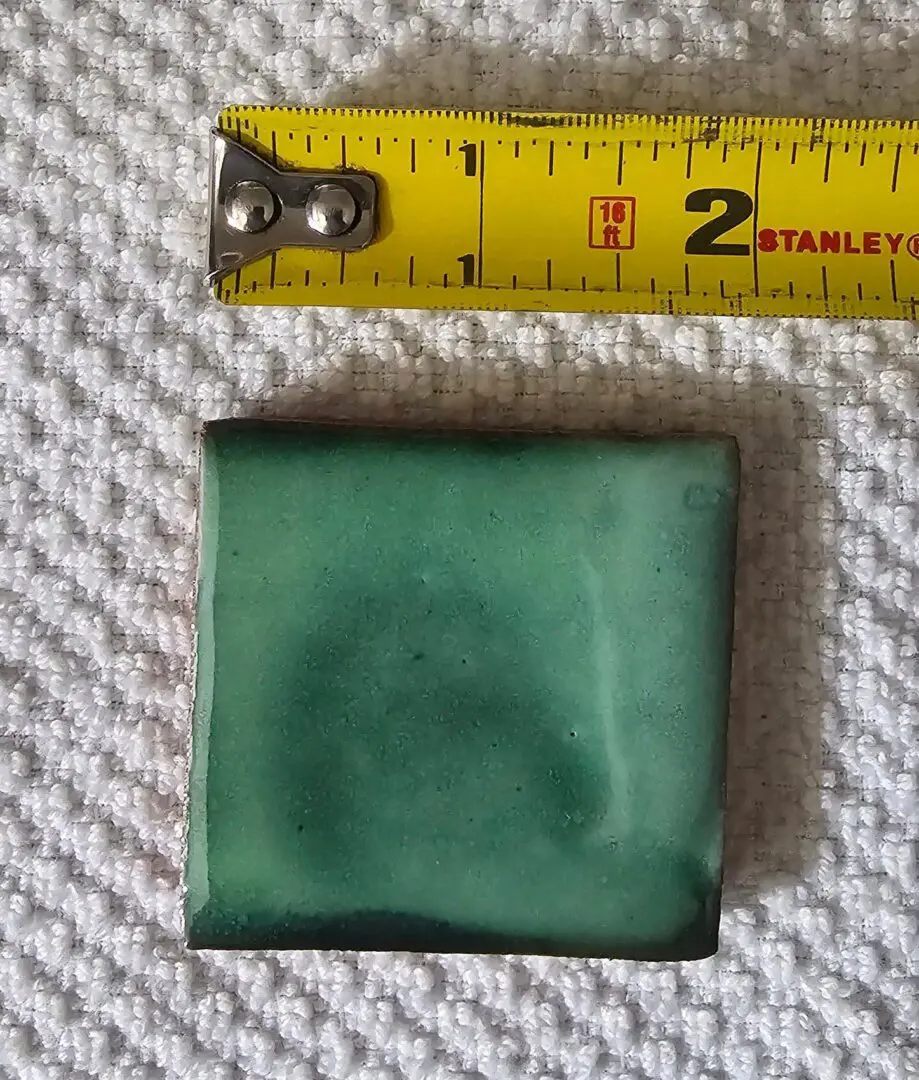 Square green jade stone next to a measuring tape showing about 2 inches.