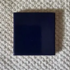 A small, dark blue square tile on a textured surface.