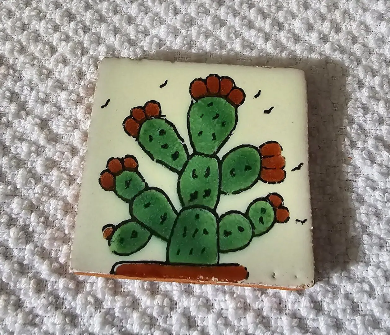 A hand-painted tile featuring a green cactus with red flowers in a brown pot.