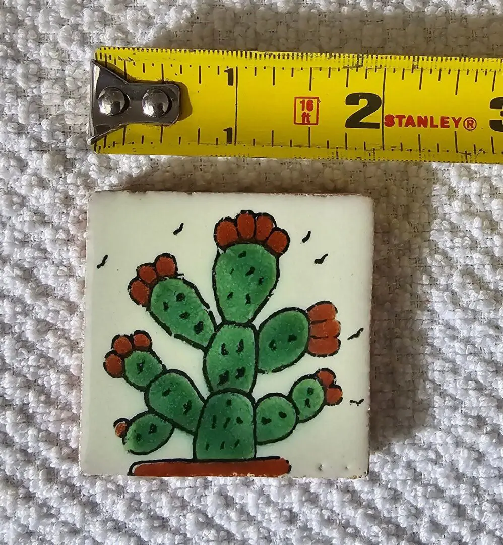 Small ceramic tile with painted cactus and measuring tape.