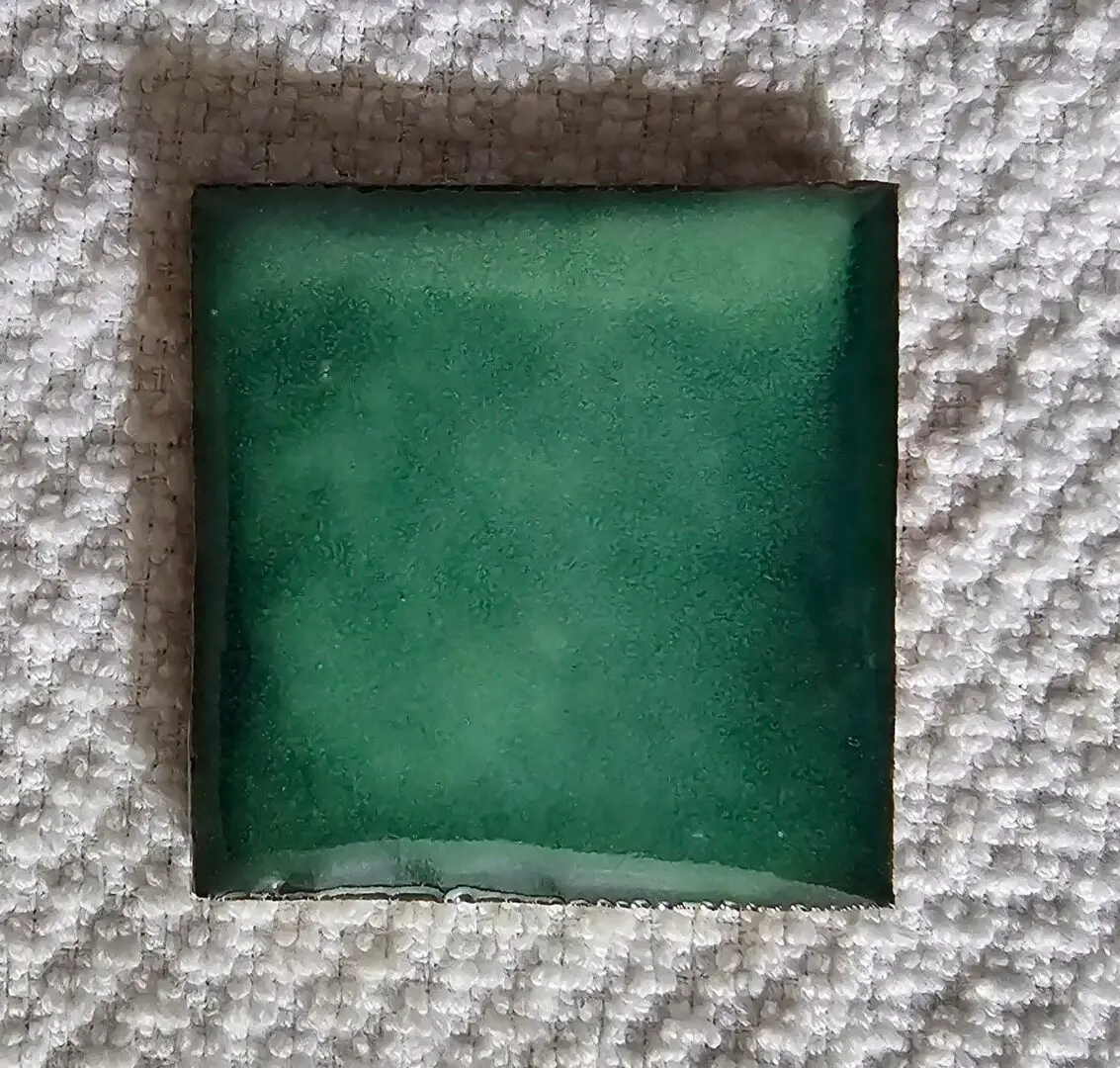 A single green ceramic tile on a textured surface.