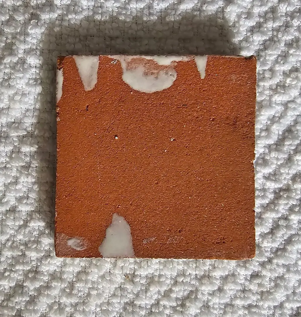 A small, worn ceramic tile with chipped edges on a textured fabric surface.