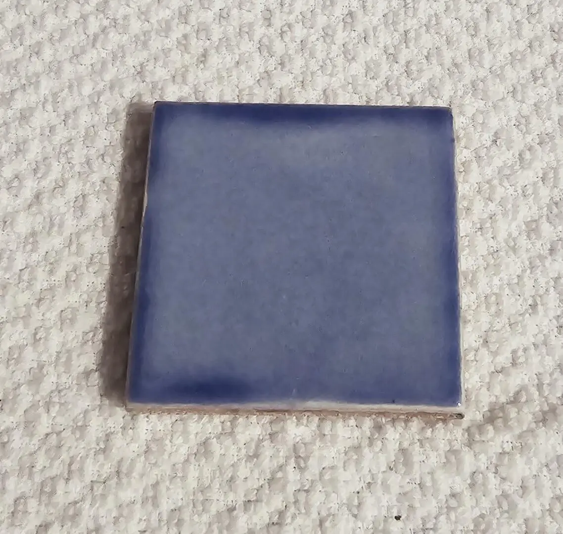 Small square blue ceramic tile on textured surface