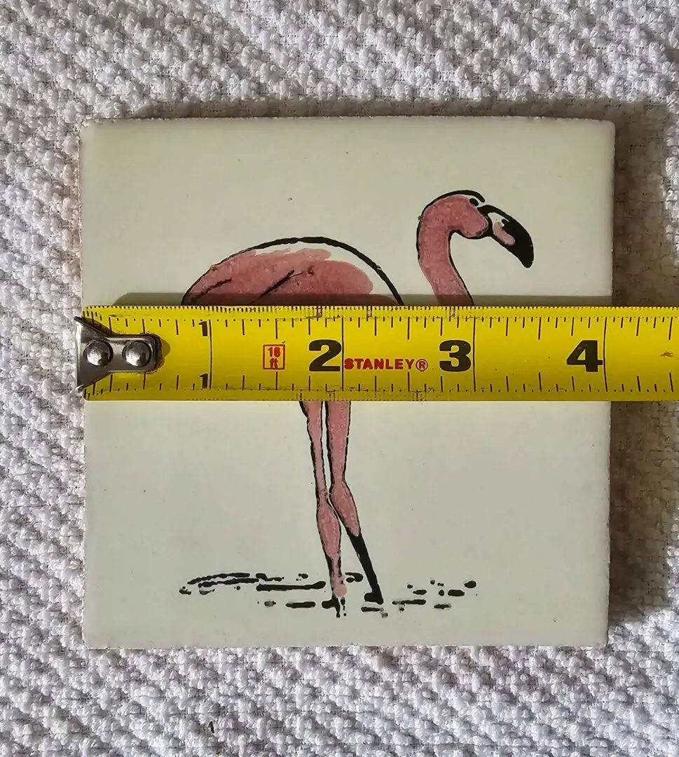 Tile with flamingo, yellow measuring tape across.