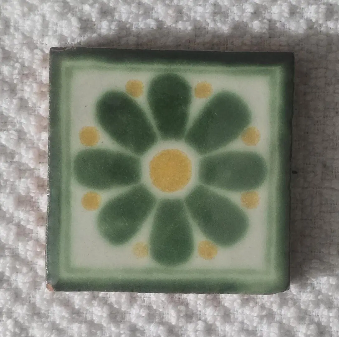 A decorative tile with a green flower and yellow center.