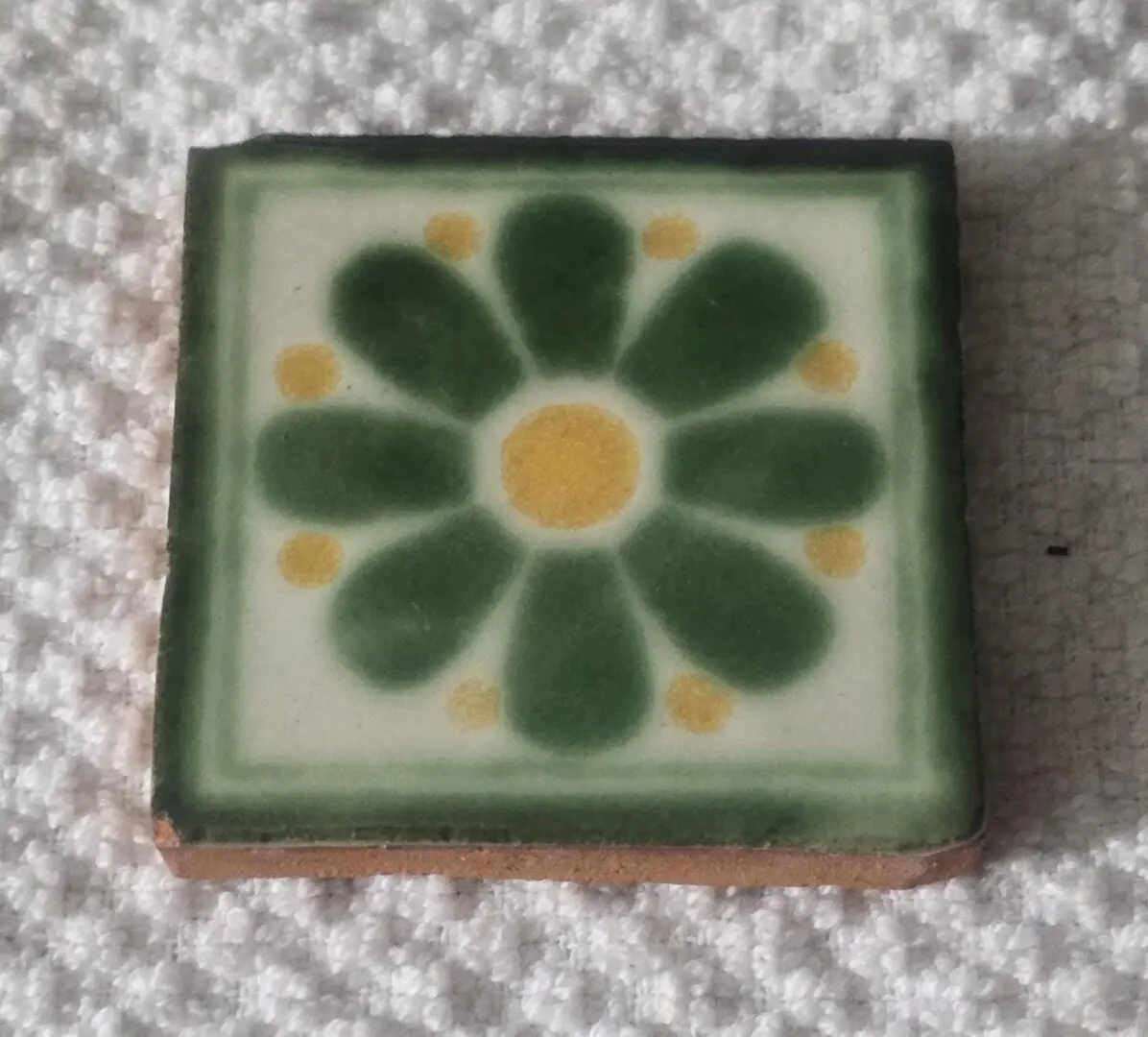 Decorative tile with a green and yellow flower pattern.