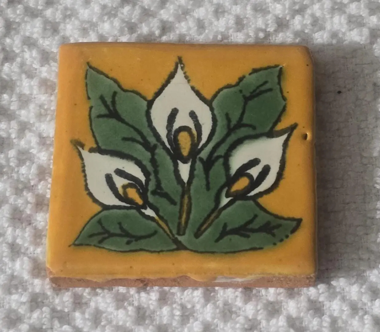 Decorative tile with white calla lilies on a mustard yellow background.
