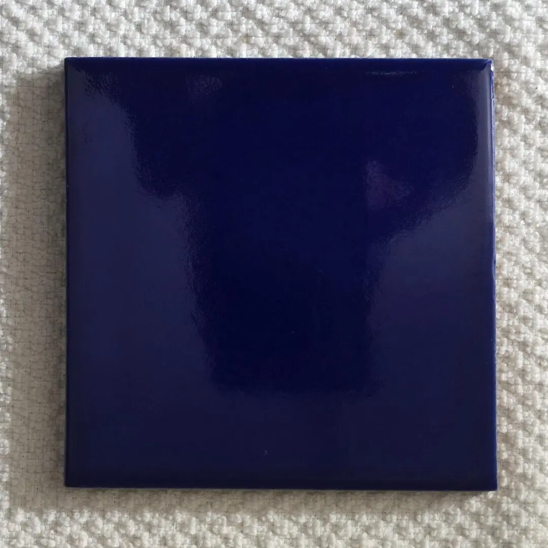 A shiny, dark blue ceramic tile on a textured fabric surface.
