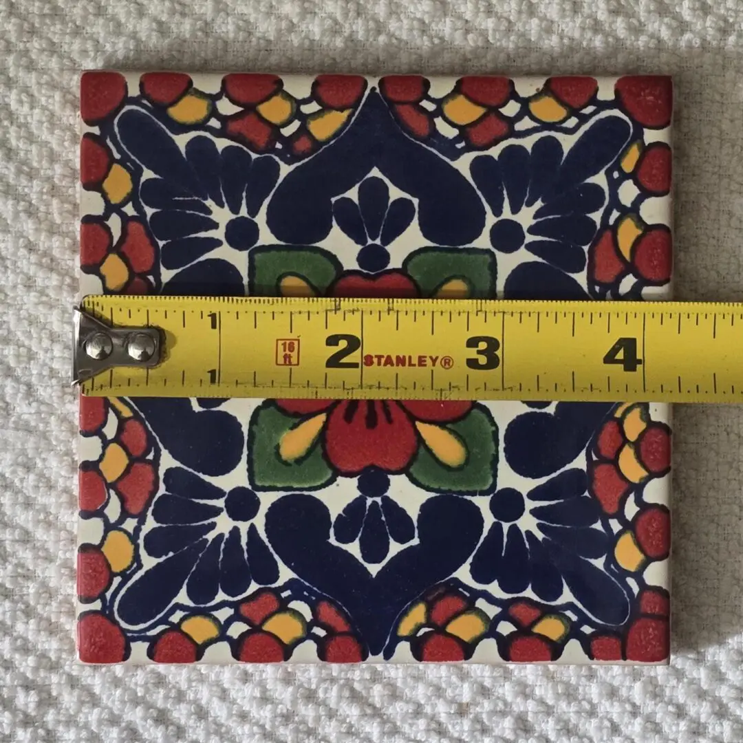 Colorful ceramic tile with floral patterns under measurement tape.
