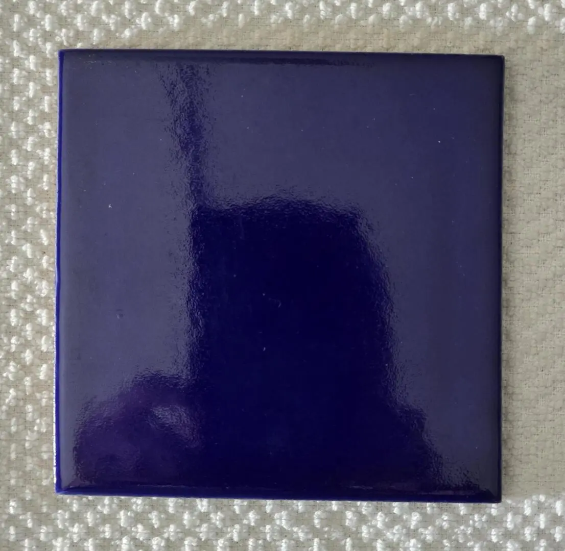 A glossy dark blue square tile on a textured light surface.