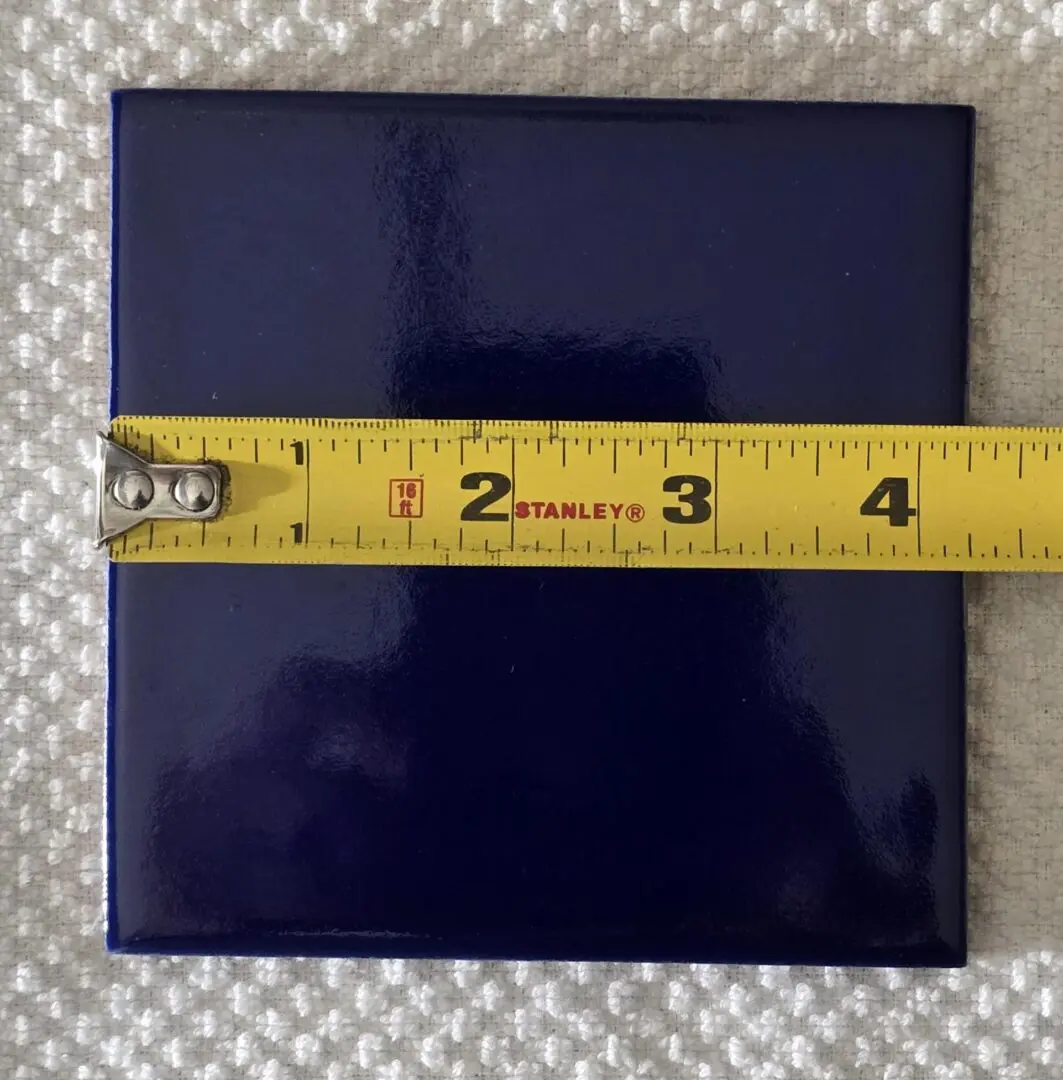 Measuring a square blue tile with a tape measure.