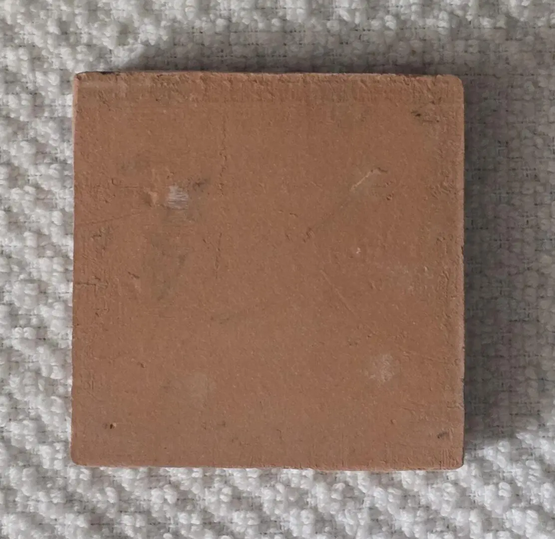 Small square terracotta tile on textured fabric