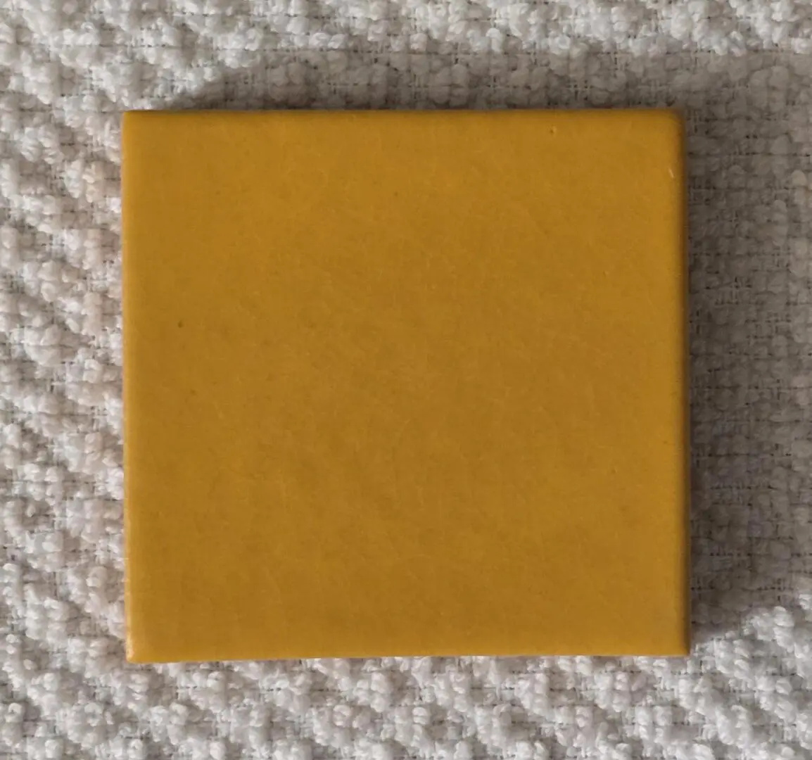 Yellow square tile on textured surface.