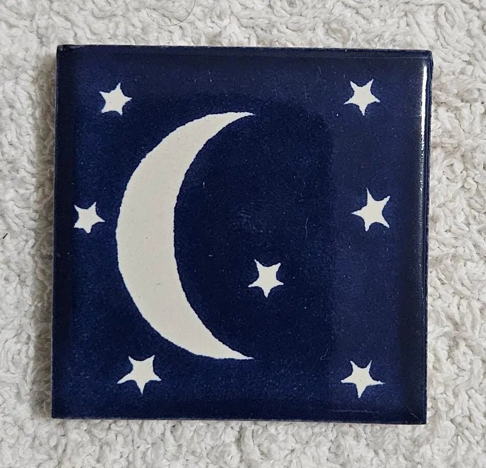 A dark blue tile with a crescent moon and stars design.