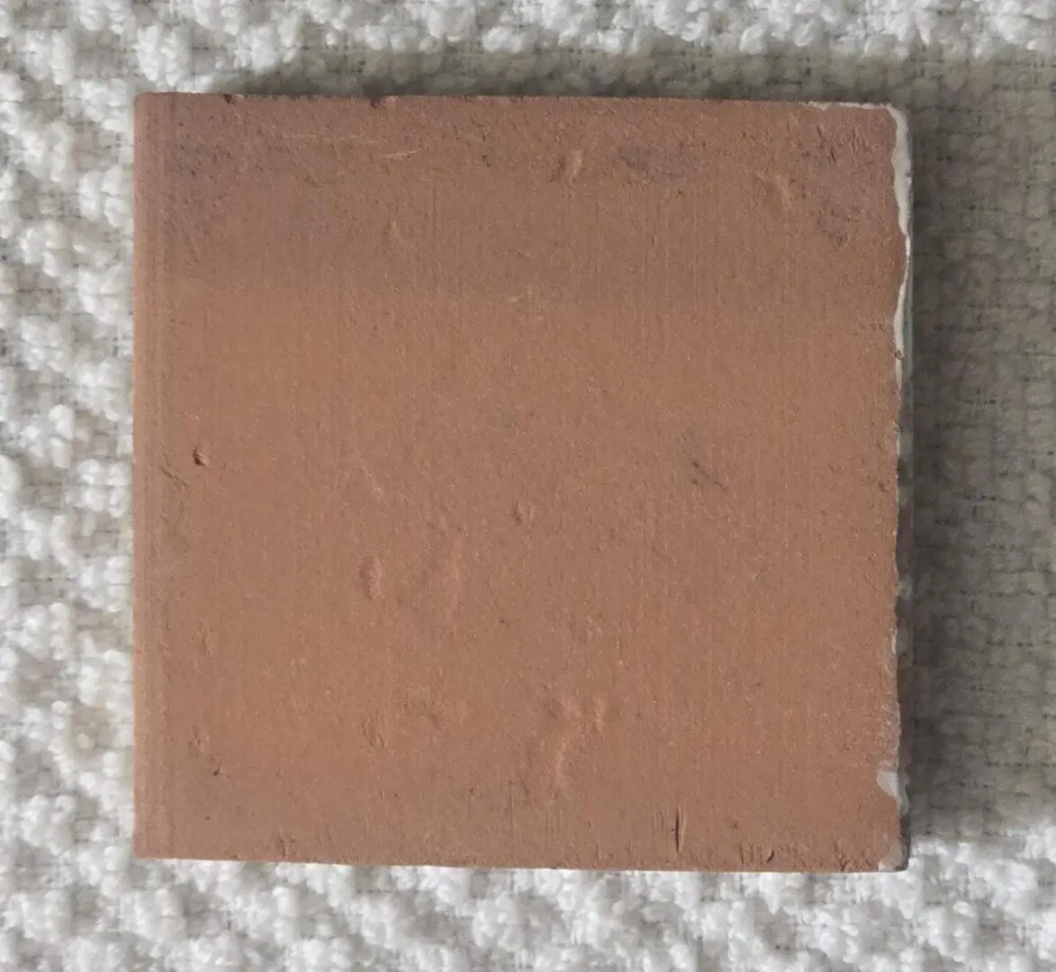 Square terracotta tile sample on textured fabric