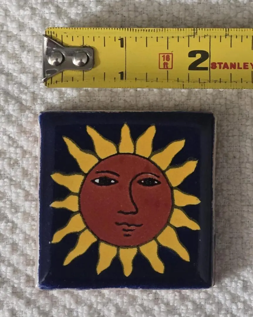 Tile with sun design, next to tape measure.