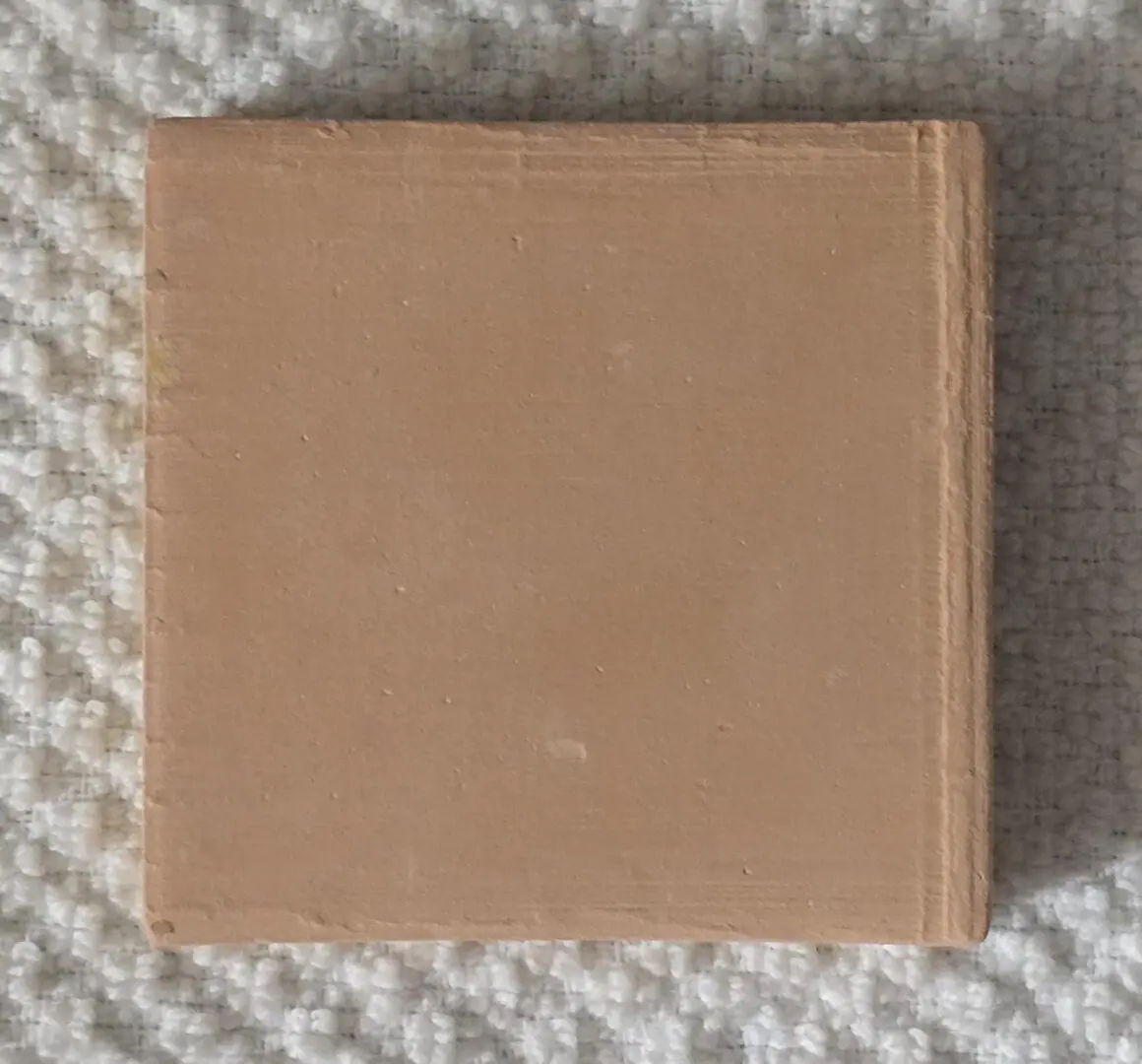 Square brown ceramic tile on textured surface.