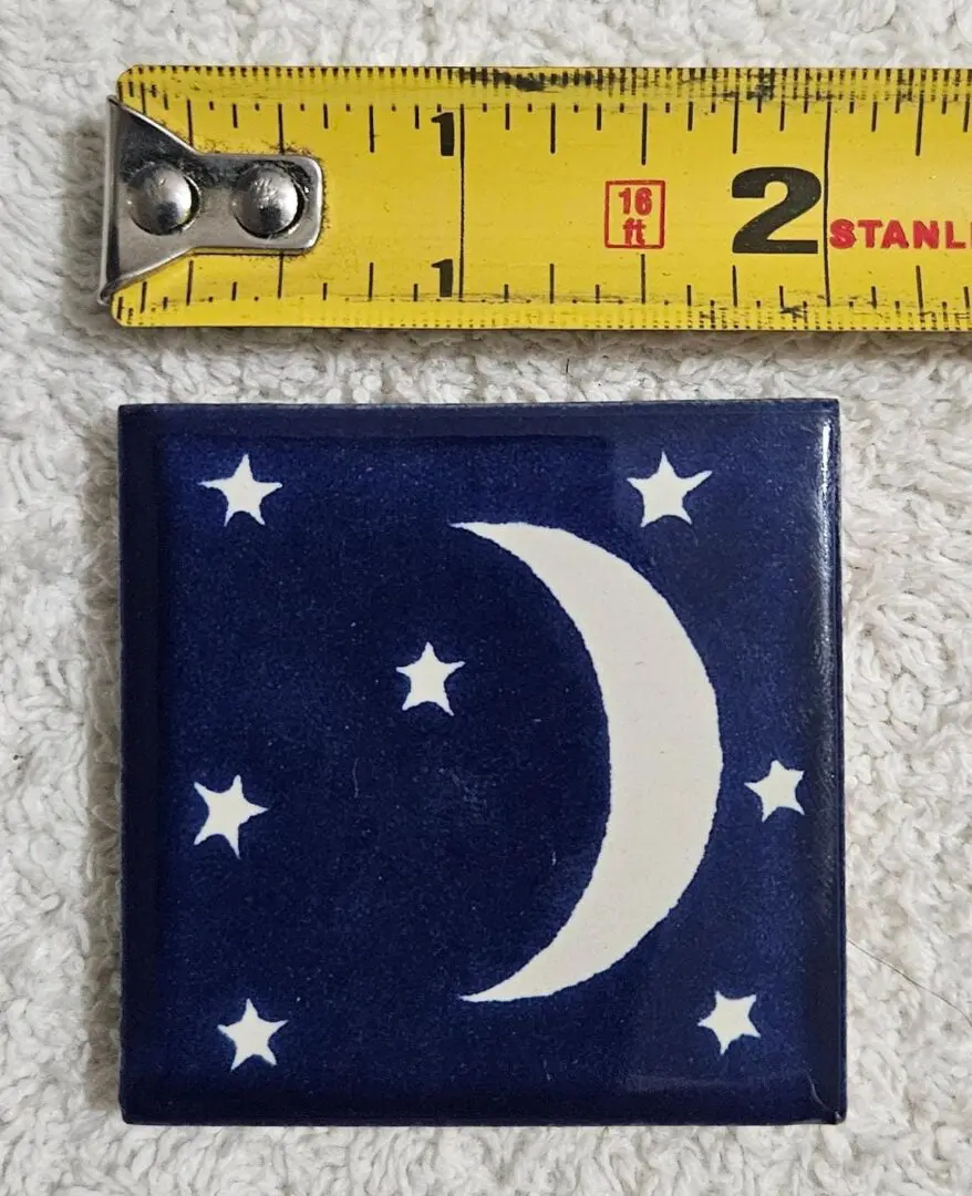 A small tile with a crescent moon and stars beside a measuring tape.