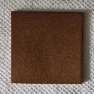 A square brown tile placed on a textured surface.
