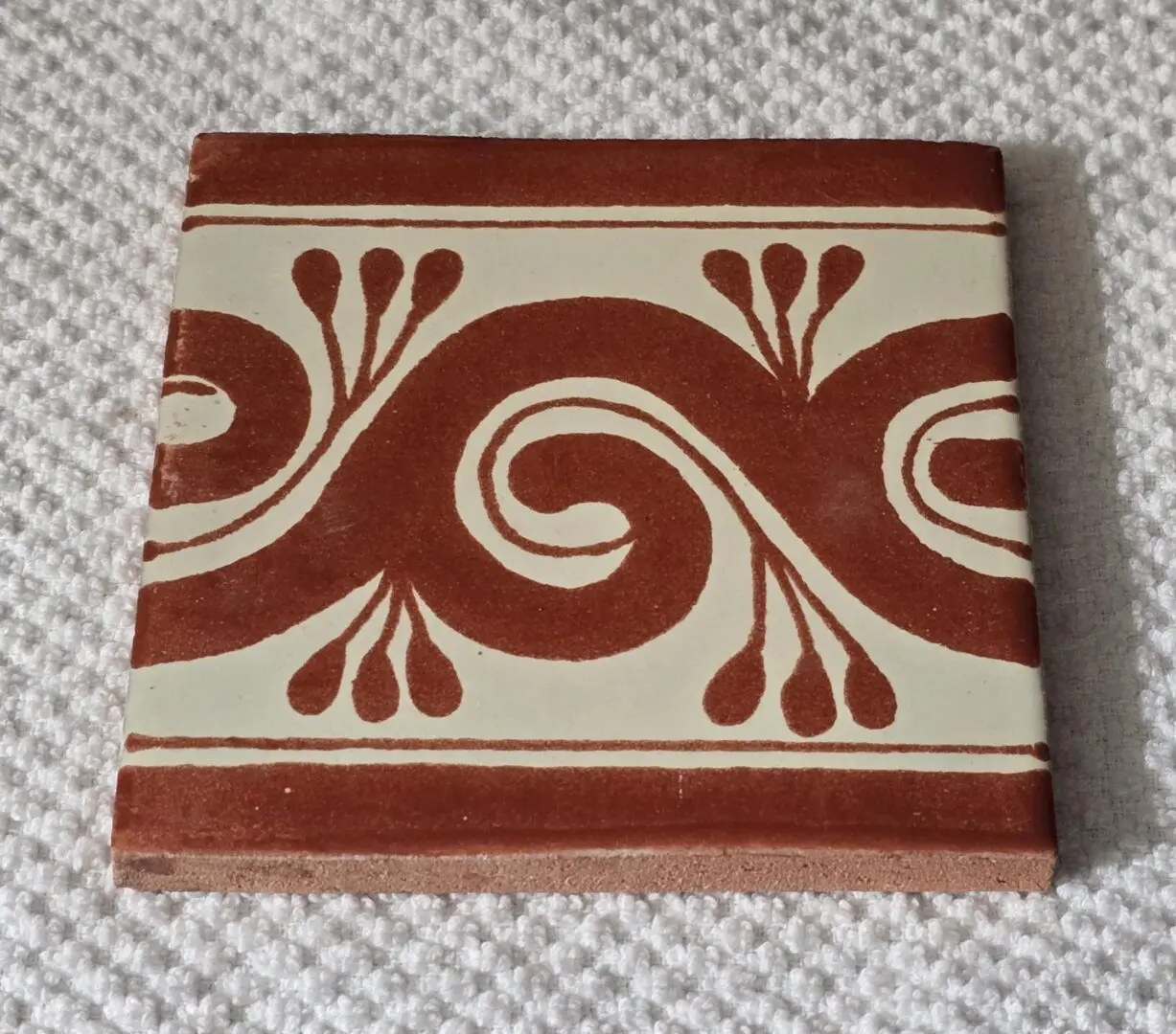 Decorative ceramic tile with red swirl pattern.