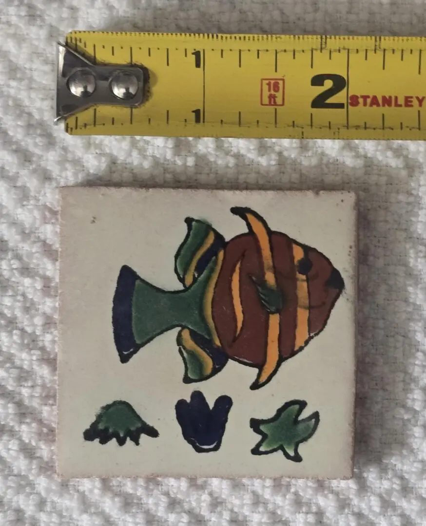 Small tile with fish design and ruler.