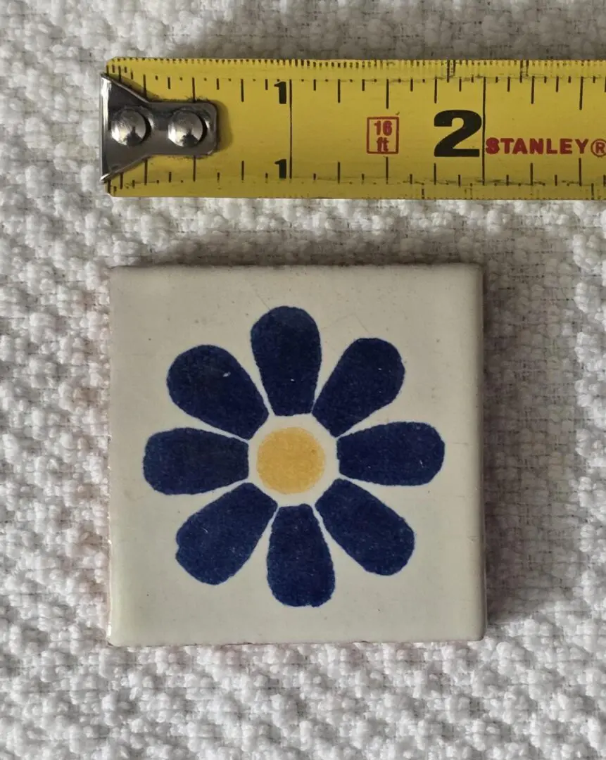 Tile with blue flower beside measuring tape.