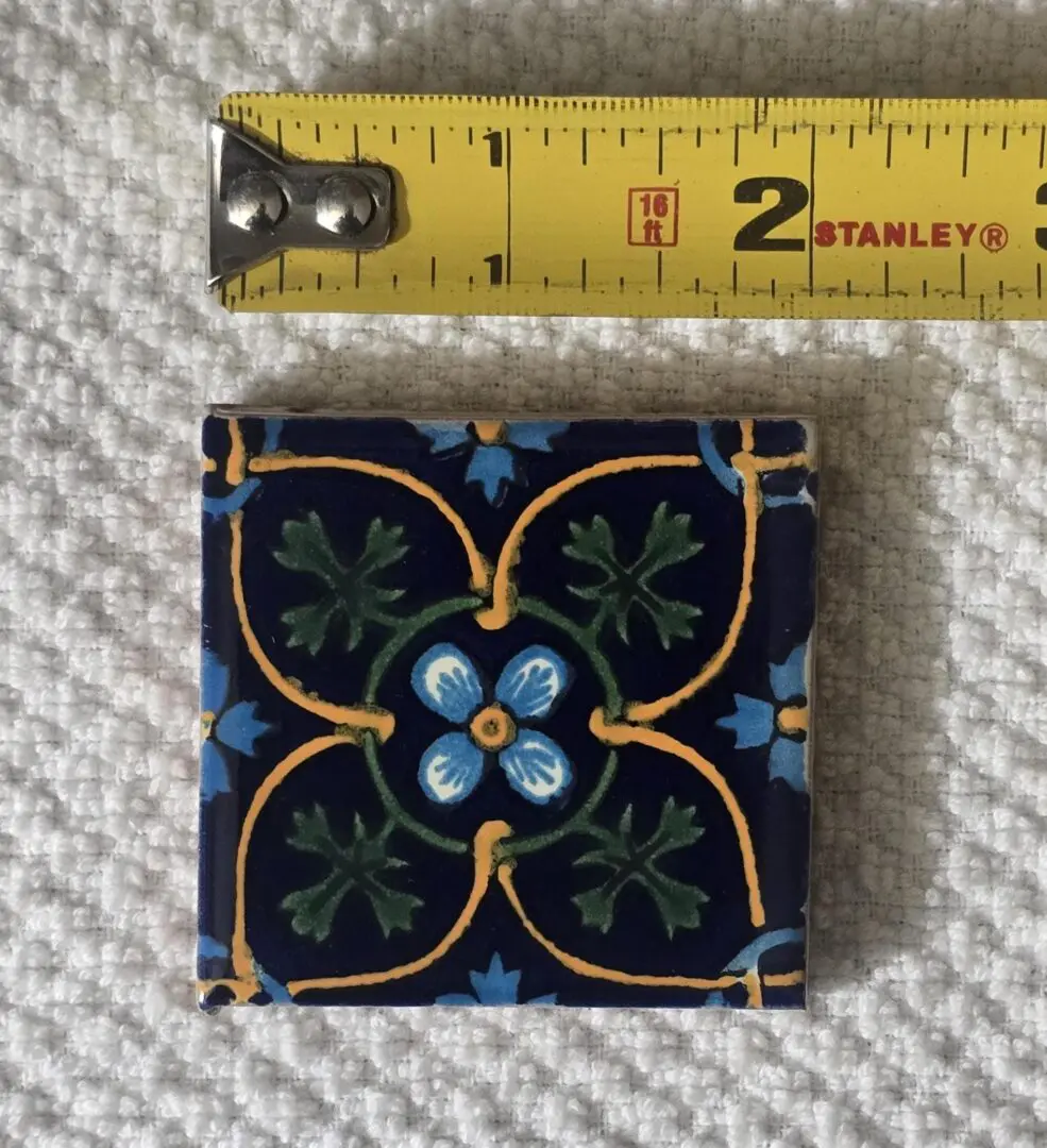Small decorative tile with blue and green floral patterns and a yellow border.