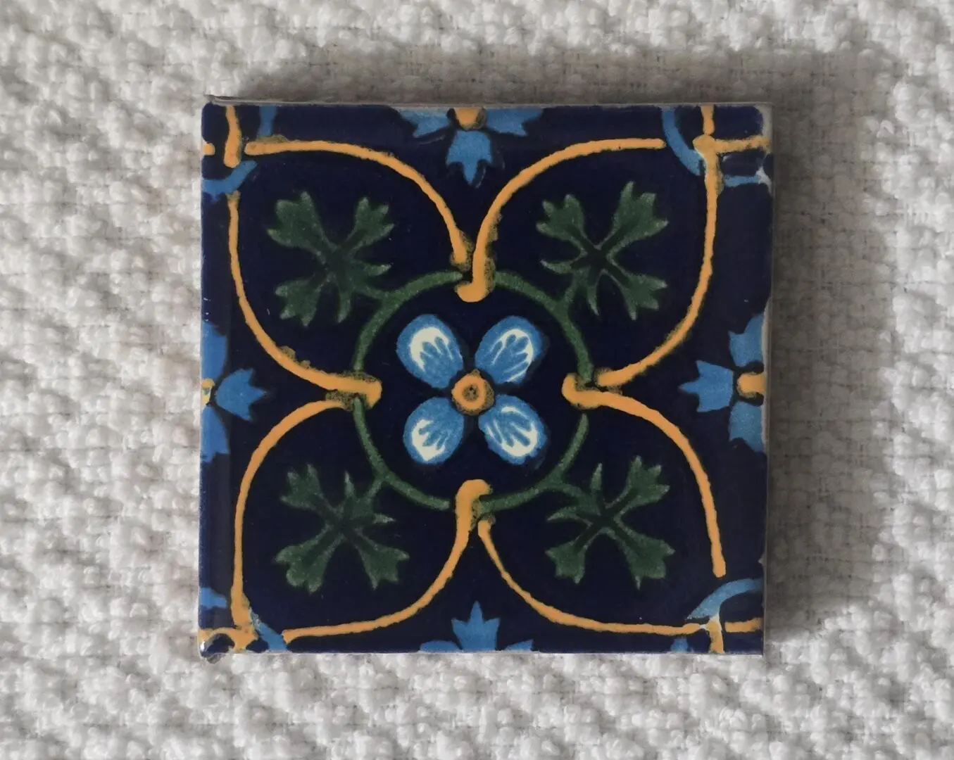Decorative square tile with blue, green, and yellow floral pattern.