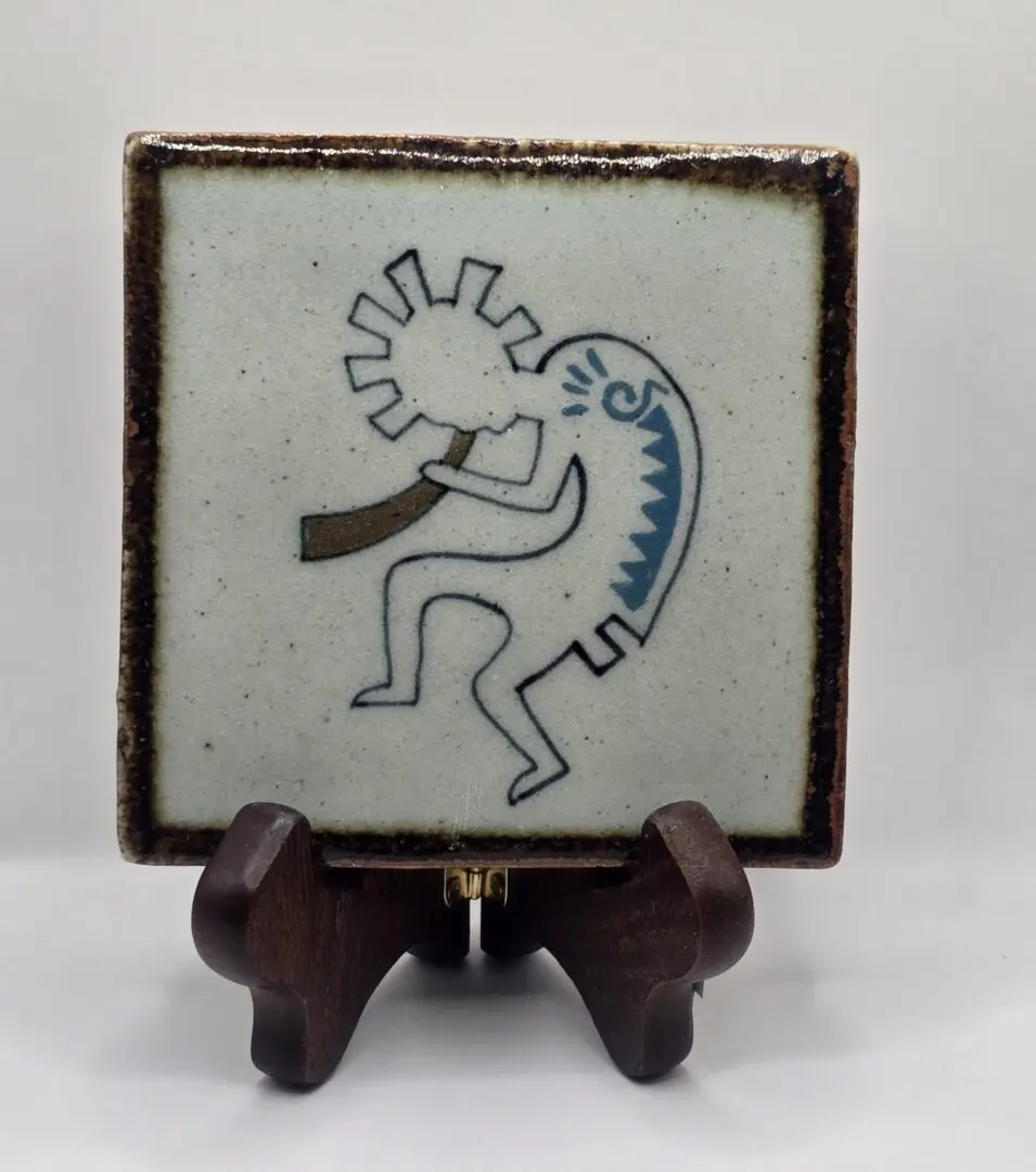 Tile with abstract figure on wooden stand.