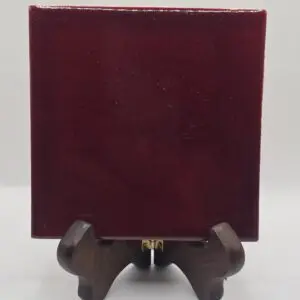 A burgundy square tile displayed on a small wooden stand.