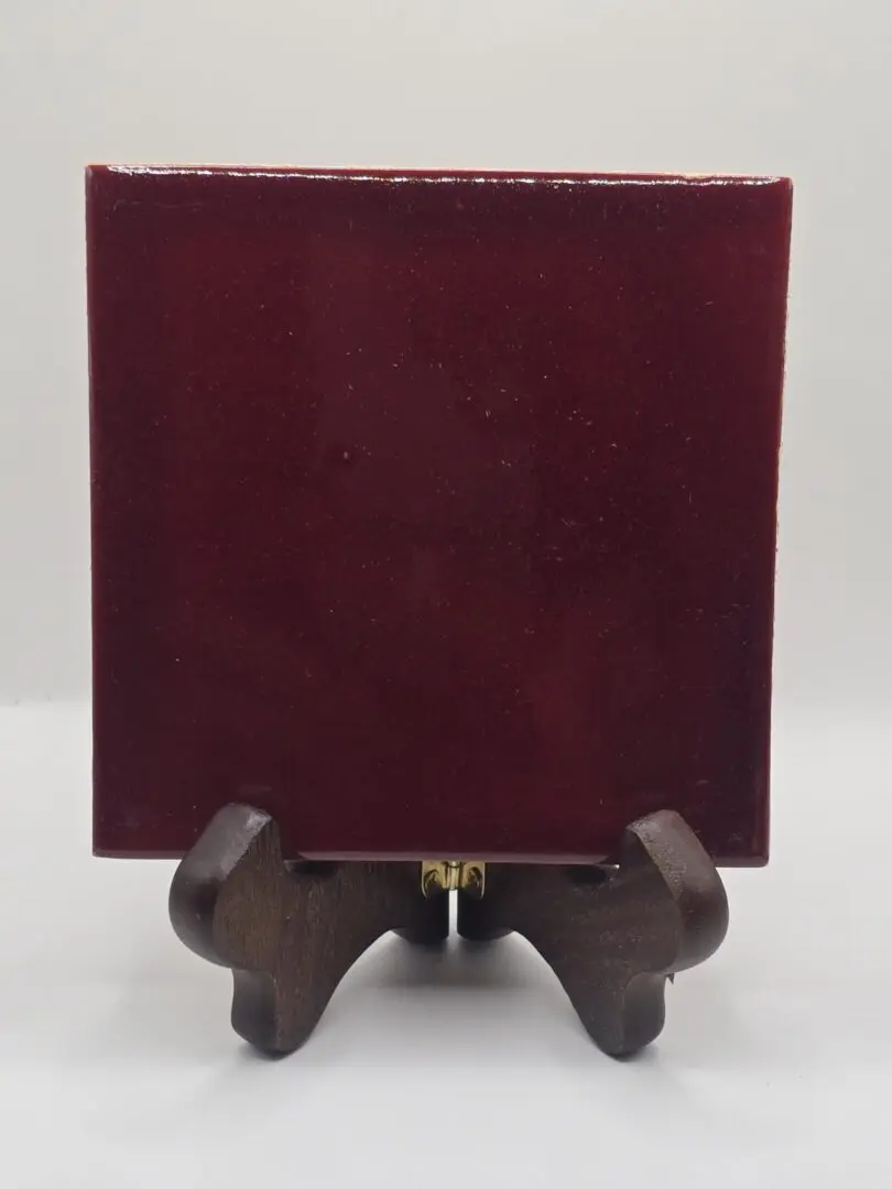 A burgundy square tile displayed on a small wooden stand.
