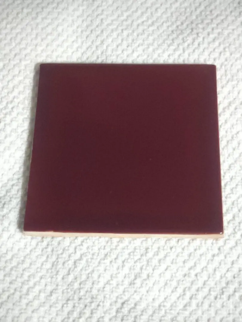 A single square maroon tile on a textured white surface.