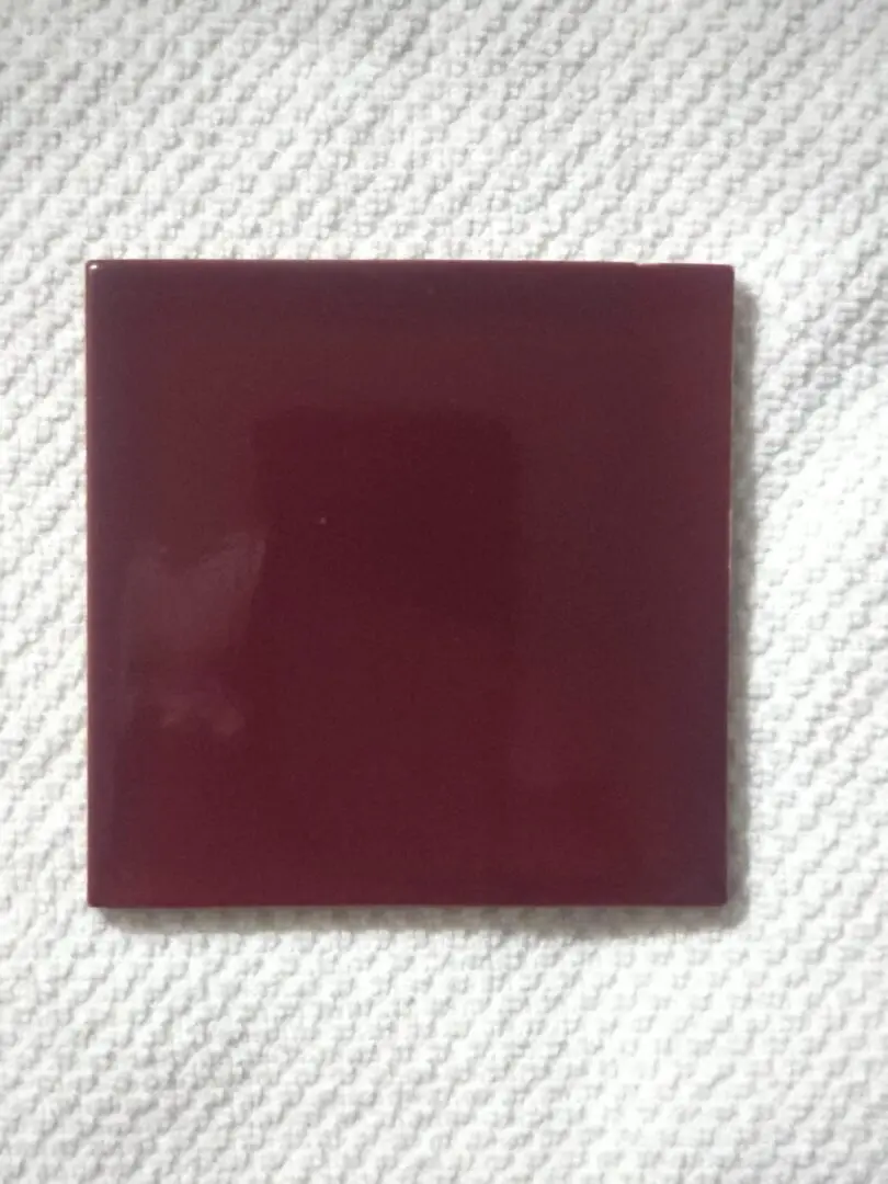 A dark burgundy square tile on a textured white surface.