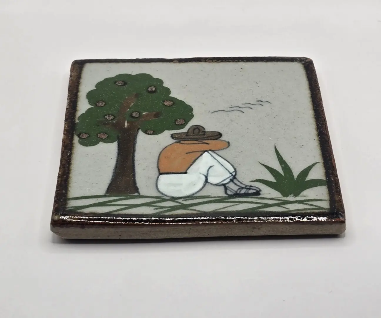 Tile with man sitting under a tree.