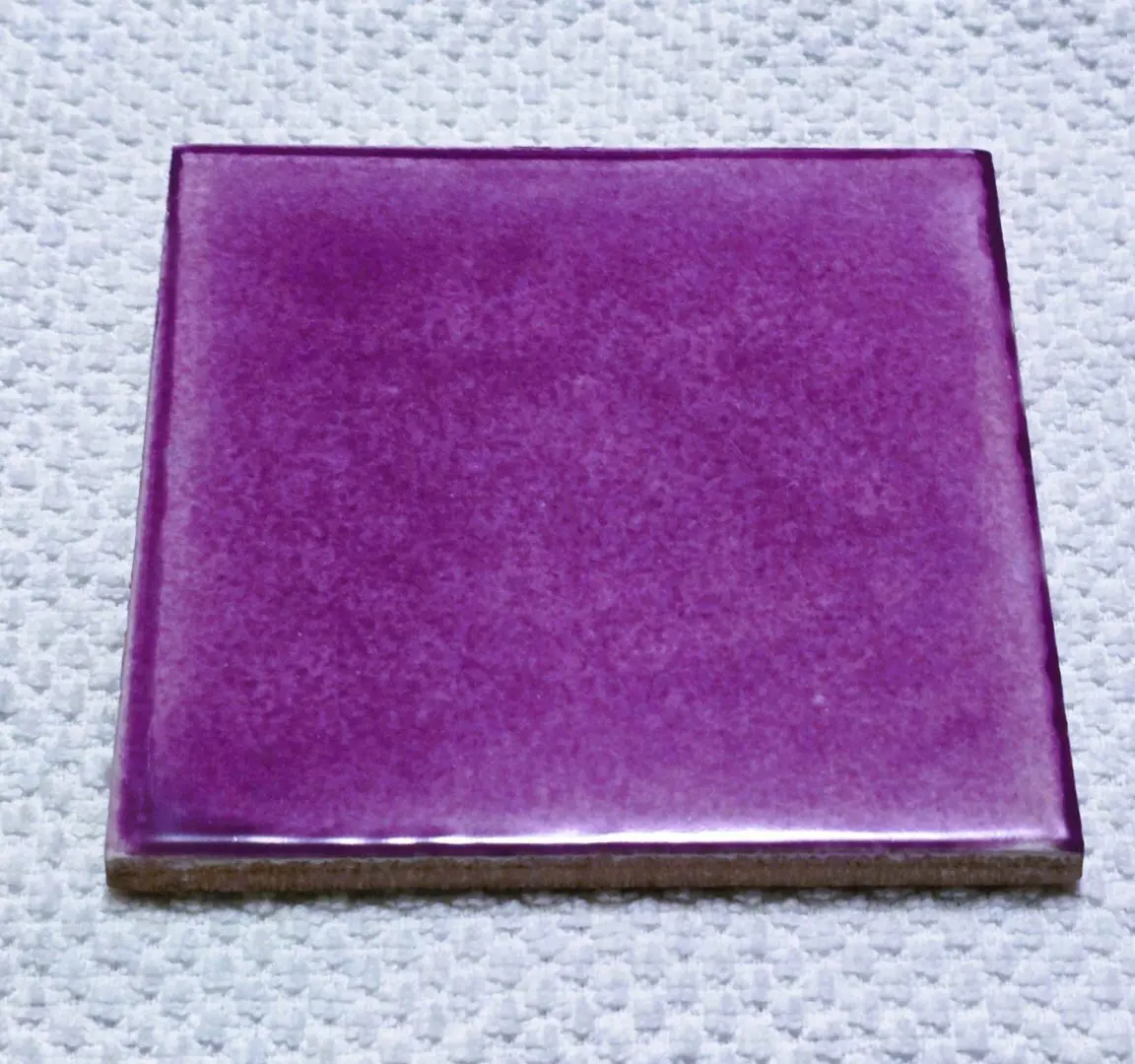 Purple ceramic tile on textured surface.