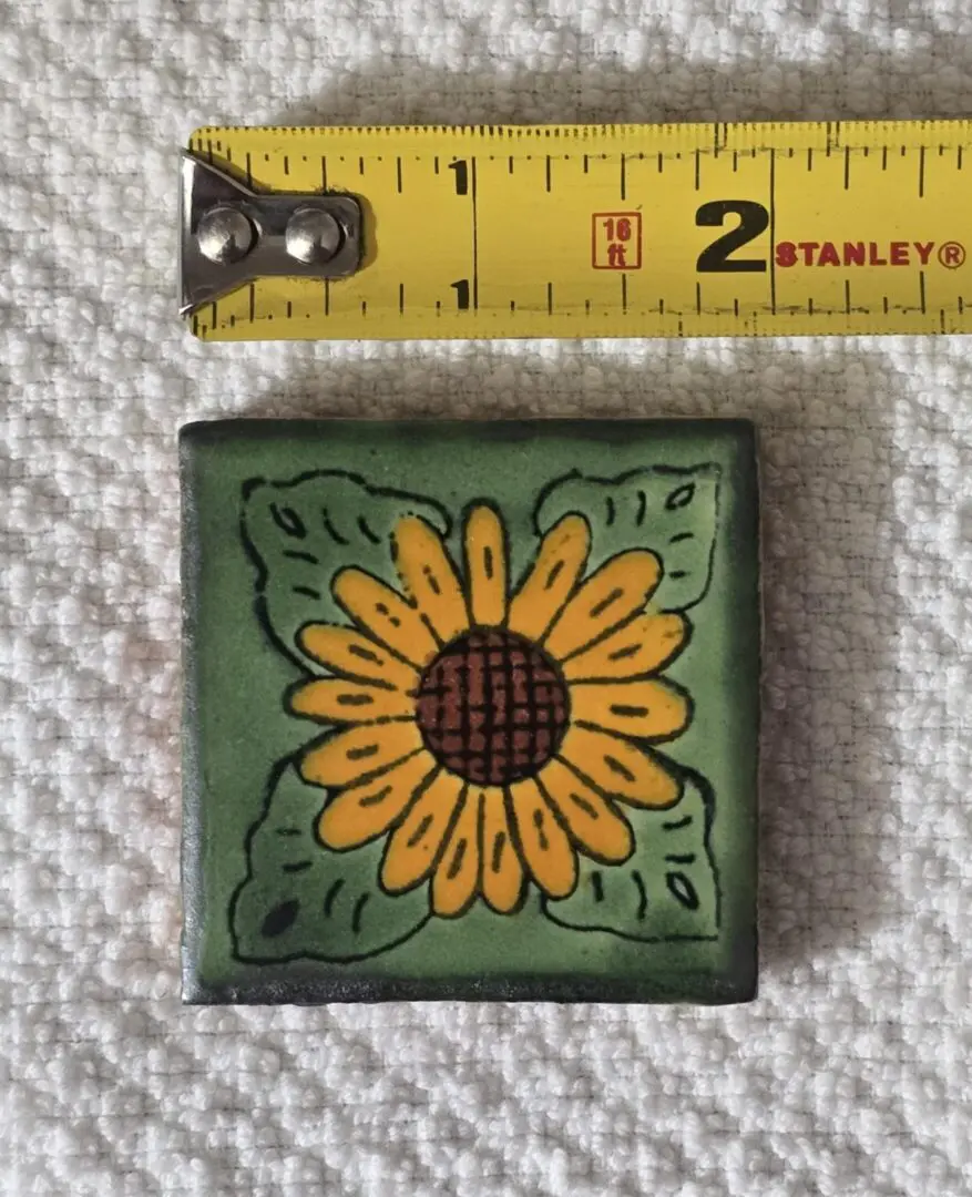 Small sunflower tile next to measuring tape.